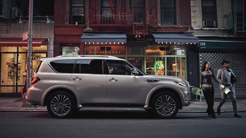 A gray 2021 Infiniti QX80 parked on the sidewalk where the driver and passenger are walking away to their destination