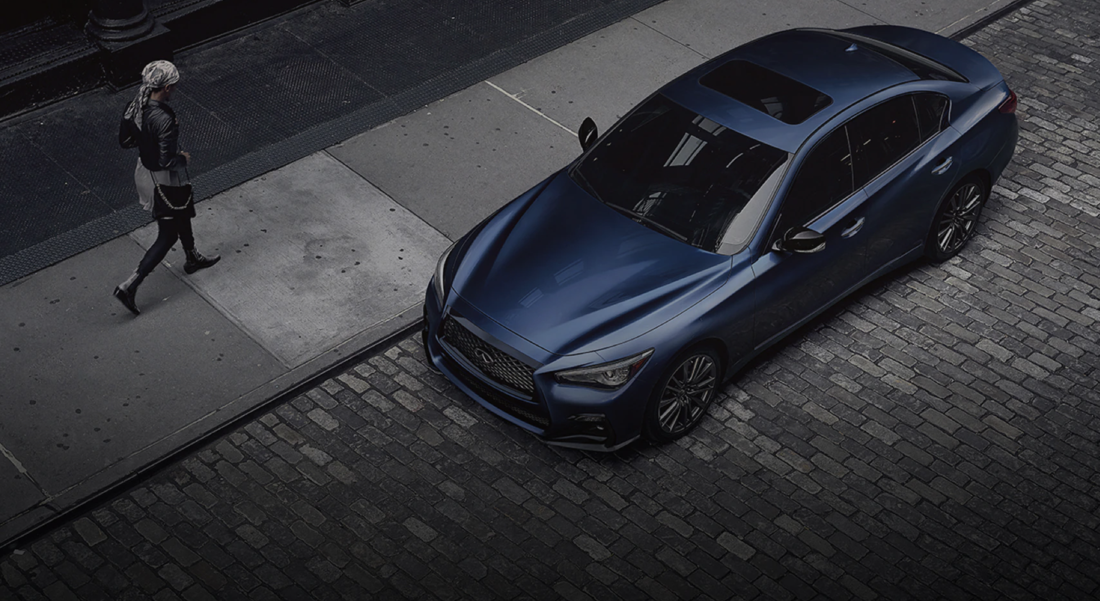 A blue 2021 model Infiniti Q50 parked on the street next to a sidewalk