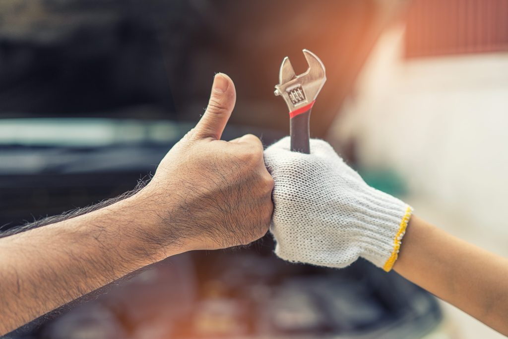 Hands giving a thumbs-up and holding a wrench in front of an open car hood