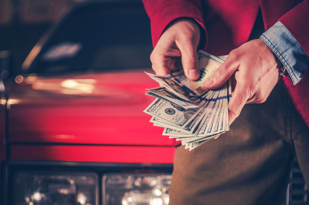 Person holding cash in front of a car, representing car trade-in