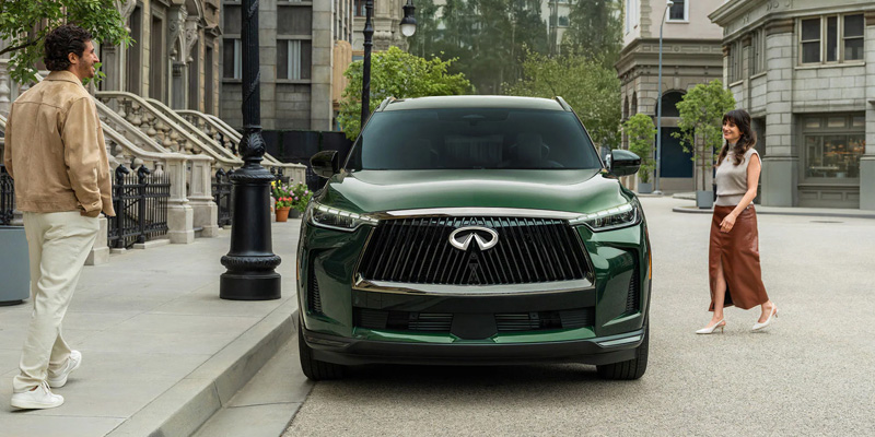 Green Infiniti SUV parked on a city street with two pedestrians standing nearby in an urban setting.