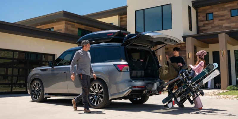Two individuals placing skis into the trunk of an SUV in a snowy outdoor setting.